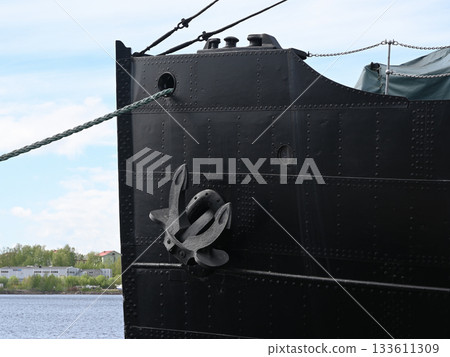 the imposing bow of a large black ship moored at a harbor, featuring a prominent steel anchor attached to its riveted metal hul the imposing bow of a large black ship moored at a harbor, featuring a prominent steel anchor attached to its riveted metal hul 133611309