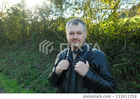 40 year old man in leather jacket walking in nature in early autumn, looking at camera, place for text. 40 year old man in leather jacket walking in nature in early autumn, looking at camera, place for text. 133611358
