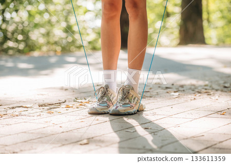 Legs of young woman that is using jumping rope. Outdoors, sunlight, close up view Legs of young woman that is using jumping rope. Outdoors, sunlight, close up view 133611359