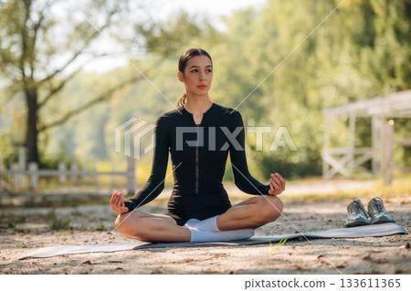 Healthcare concept, doing exercises. Young sportive skinny woman is in black fitness clothes outdoors 133611365