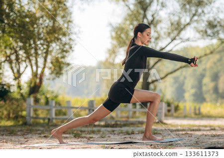Doing yoga exercises. Young sportive skinny woman is in black fitness clothes outdoors Doing yoga exercises. Young sportive skinny woman is in black fitness clothes outdoors 133611373