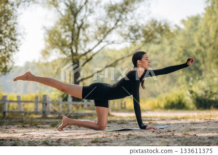 Doing yoga exercises. Young sportive skinny woman is in black fitness clothes outdoors 133611375