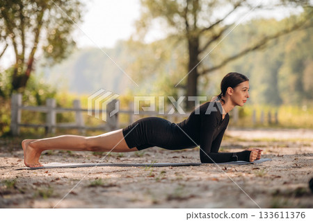 Doing yoga exercises. Young sportive skinny woman is in black fitness clothes outdoors Doing yoga exercises. Young sportive skinny woman is in black fitness clothes outdoors 133611376