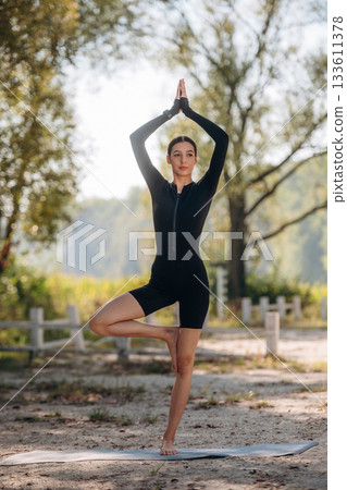Doing yoga exercises. Young sportive skinny woman is in black fitness clothes outdoors Doing yoga exercises. Young sportive skinny woman is in black fitness clothes outdoors 133611378