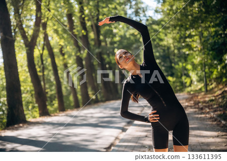 Warm up exercises. Young sportive skinny woman is in black fitness clothes outdoors 133611395