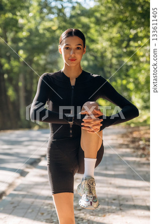 Legs warm up. Young sportive skinny woman is in black fitness clothes outdoors Legs warm up. Young sportive skinny woman is in black fitness clothes outdoors 133611405