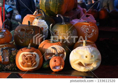 a pile of pumpkins in various shades of orange and white, with one prominently carved jack-o-lantern featuring a spooky, smiling face 133611520