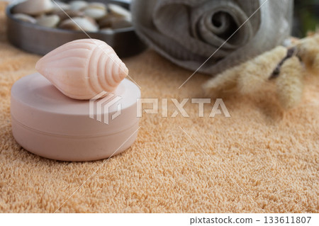 Self care treatment products on a soft orange towel adorned with seashells and dried lagurus grass, designed to promote relaxation and wellness. 133611807