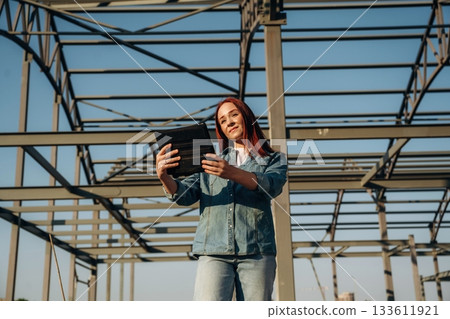 Young redhead woman is standing near unfinished building, construction Young redhead woman is standing near unfinished building, construction 133611921
