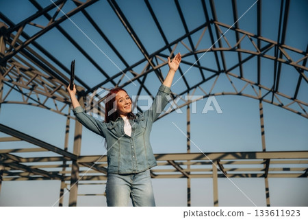 Young redhead woman is standing near unfinished building, construction Young redhead woman is standing near unfinished building, construction 133611923