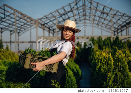 Side view, holding box with plants. Young redhead woman is taking care of garden Side view, holding box with plants. Young redhead woman is taking care of garden 133611937