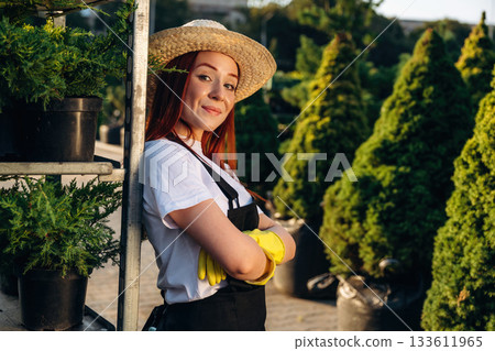 In straw hat. Young redhead woman is taking care of garden 133611965