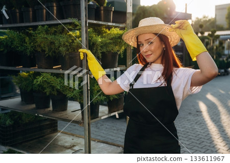 In straw hat. Young redhead woman is taking care of garden In straw hat. Young redhead woman is taking care of garden 133611967