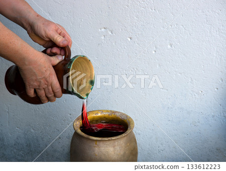 A hand holds a clay jar and pours water A hand holds a clay jar and pours water 133612223