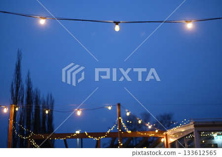 Soft, warm string lights glow against a deep blue evening sky Soft, warm string lights glow against a deep blue evening sky 133612565