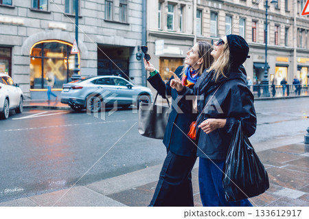 Two female friends are walking through city streets and looking at shop windows 133612917