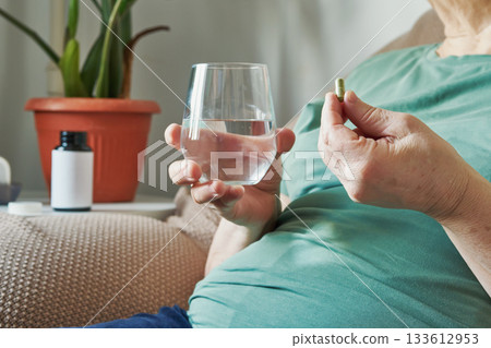 Senior woman with overweight taking daily medicine or supplement with a glass of water at home Senior woman with overweight taking daily medicine or supplement with a glass of water at home 133612953