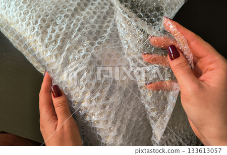 Woman is holding a plastic bubble wrap for things. Packing of things and goods Woman is holding a plastic bubble wrap for things. Packing of things and goods 133613057