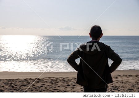 Silhouette of a man standing with his hands on his hips and looking out at the sea Silhouette of a man standing with his hands on his hips and looking out at the sea 133613135