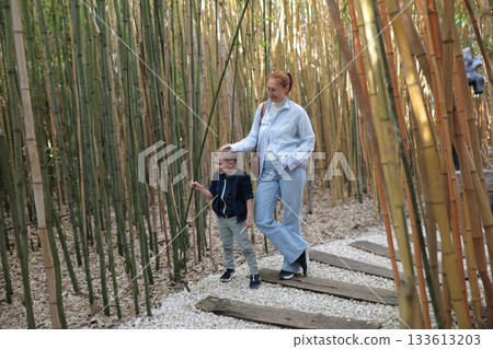 Mother and son walking pathway through bamboo garden 133613203