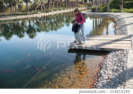 Mother and son watching koi fish in park pond Mother and son watching koi fish in park pond 133613240
