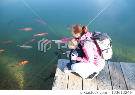Mother and son watching fish in clear lake water Mother and son watching fish in clear lake water 133613246