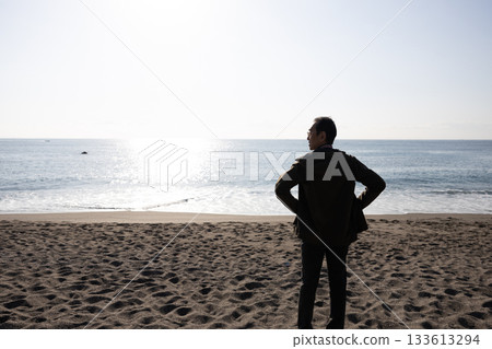 Silhouette of a man standing with his hands on his hips and looking out at the sea Silhouette of a man standing with his hands on his hips and looking out at the sea 133613294