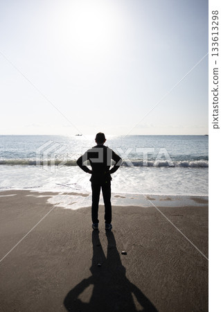 Silhouette of a man standing with his hands on his hips and looking out at the sea Silhouette of a man standing with his hands on his hips and looking out at the sea 133613298