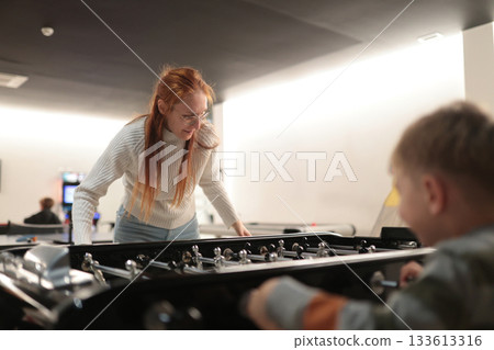 Woman and boy playing competitive foosball game indoors 133613316