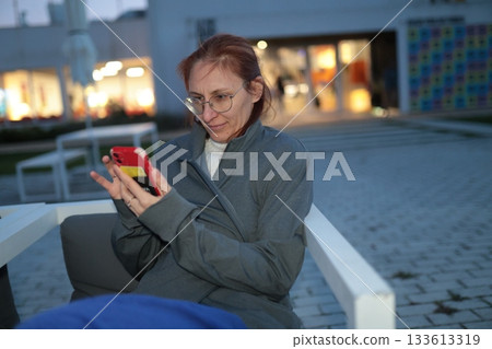 Woman watching content on smartphone outdoors at dusk Woman watching content on smartphone outdoors at dusk 133613319