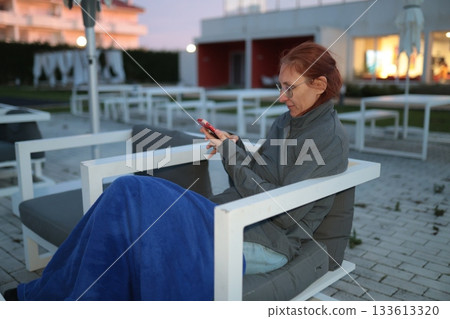 Woman relaxing outdoors using smartphone at hotel resort Woman relaxing outdoors using smartphone at hotel resort 133613320