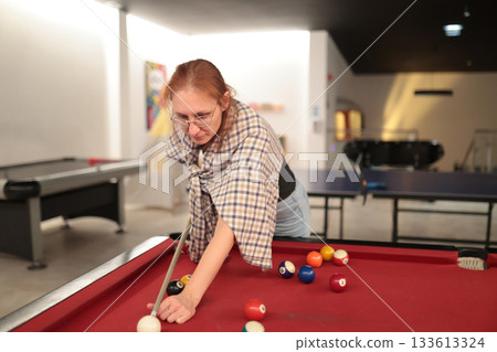 Woman playing billiards in game room 133613324
