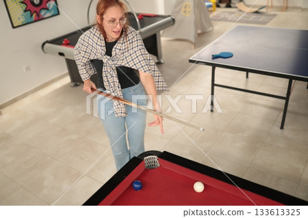 Woman playing billiards in game room concentrating on shot 133613325