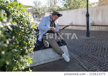 Man tying ropes on fishing rod in park Man tying ropes on fishing rod in park 133613373