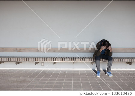 A middle-aged man sitting on a bench, holding his head and slumped 133613480