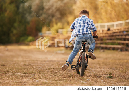 Riding, having fun. Cute boy is with his bicycle on the field 133613516
