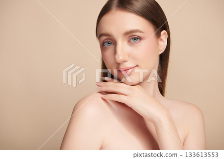 A beautiful young woman with clean, fresh skin against a beige background. Skincare, facial treatment, cosmetology, beauty, and spa. An elegant portrait of an woman. 133613553