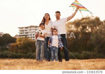 Family of father, mother, daughter and son that are standing in the field, with kite in hand 133613578