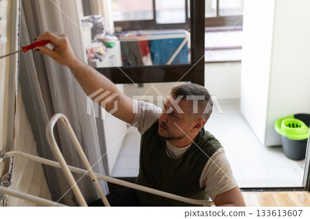 Man concentrating painting apartment wall home improvement project Man concentrating painting apartment wall home improvement project 133613607