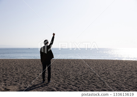 Back view of a man raising one hand towards the sea 133613619