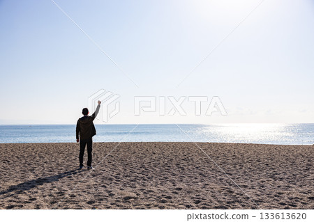 男子背對著鏡頭,舉起一隻手指向大海。 男子背對著鏡頭,舉起一隻手指向大海。 133613620