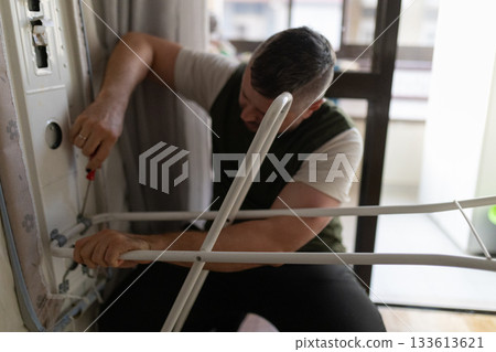Man repairing ironing board mechanism with screwdriver Man repairing ironing board mechanism with screwdriver 133613621