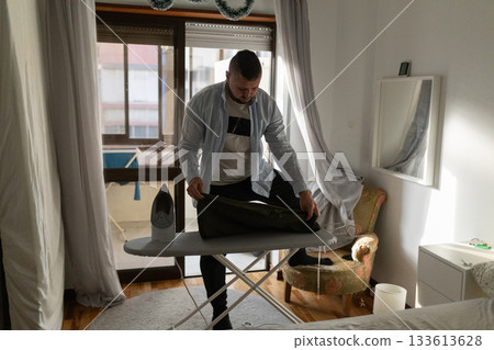 Man ironing clothes on board in bright room Man ironing clothes on board in bright room 133613628