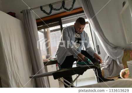Man performing household chore ironing apparel at home 133613629