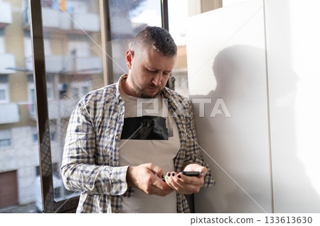 Man standing indoors checking messages on smartphone 133613630
