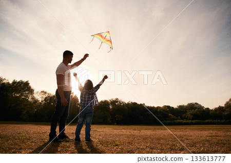 Father and son are with kite on the field, illuminated by sunlight Father and son are with kite on the field, illuminated by sunlight 133613777