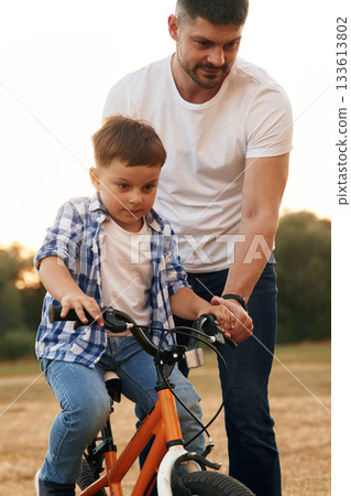 Teaching how to ride. Dad with son are with bicycle on the field outdoors 133613802