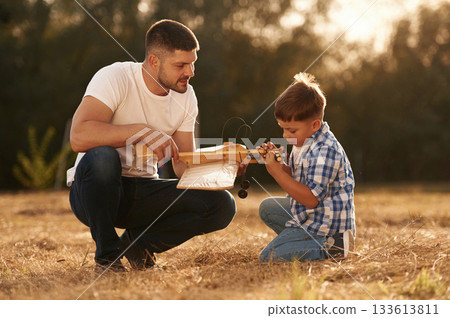 Handmade toy plane is broken, fixing it. Father and son are on the field 133613811