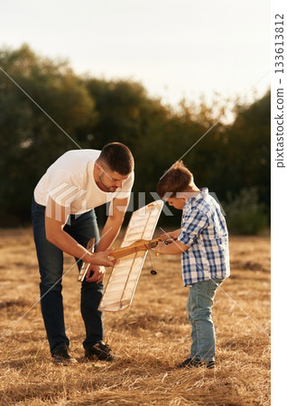 Father and son are with wooden toy plane on the field Father and son are with wooden toy plane on the field 133613812