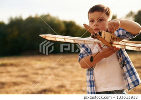 Boy is playing with wooden toy plane outdoors on the field Boy is playing with wooden toy plane outdoors on the field 133613918